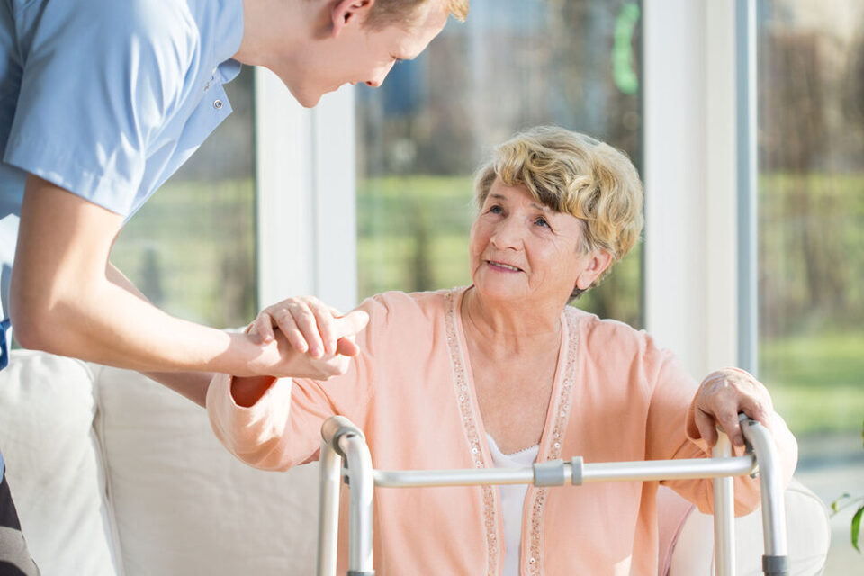 Senioren mit Gehhilfe wird unterstützt durch eine Pflegekraft