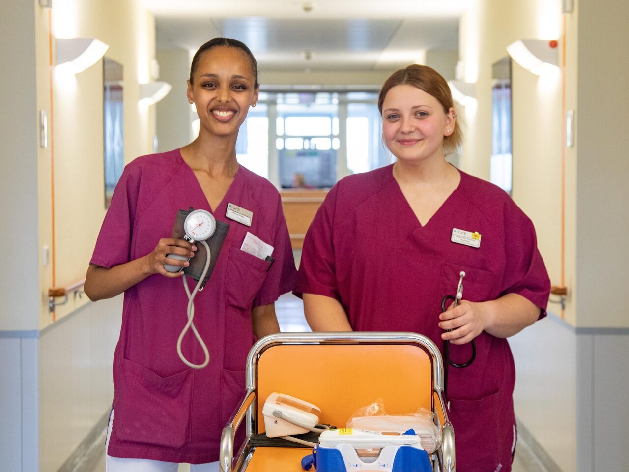 Zwei Pflegekräfte des GPR Klinikums stehen im Stationsgang und halten Blutdruckgerät und Stethoskop in der Hand