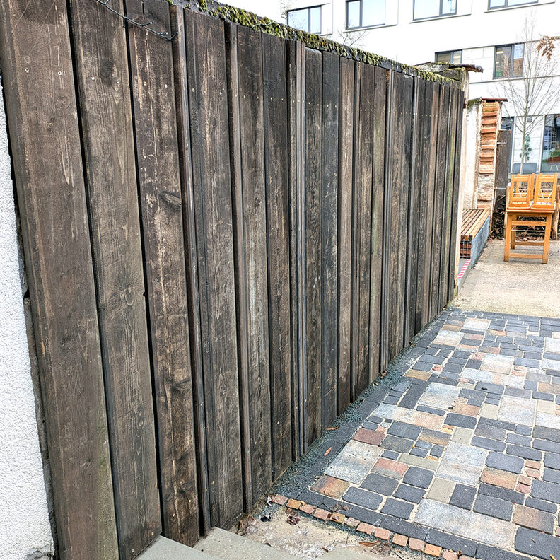 Holzverkleidung der Mauer mit Holzlatten des ehemaligen Zauns