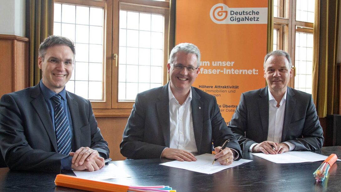 Bürgermeister Dennis Grieser, Oberbürgermeister Patrick Burghardt und Dirk Ebert (Regionalleiter Sales Deutsche GigaNetz GmbH) sitzen an einem Tisch im Rathaus und unterschreiben die Kooperationsvereinbarung (von links)