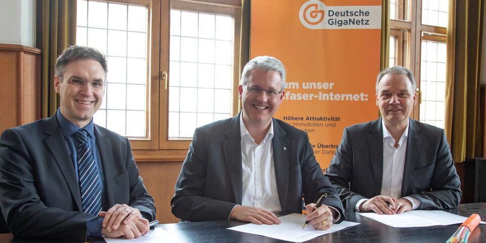 Bürgermeister Dennis Grieser, Oberbürgermeister Patrick Burghardt und Dirk Ebert (Regionalleiter Sales Deutsche GigaNetz GmbH) sitzen an einem Tisch im Rathaus und unterschreiben die Kooperationsvereinbarung (von links)