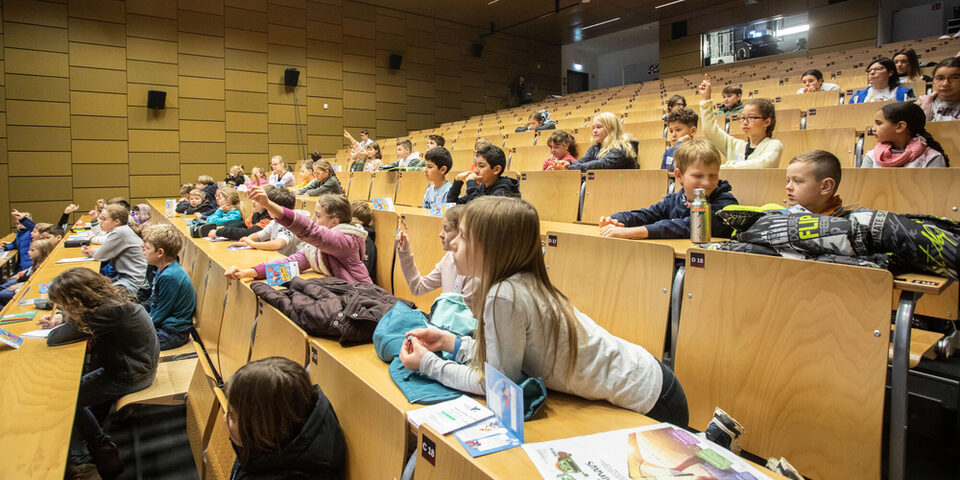 Zahlreiche Kinder hören in einem Stufenhörsaal interessiert einer Vorlesung zu