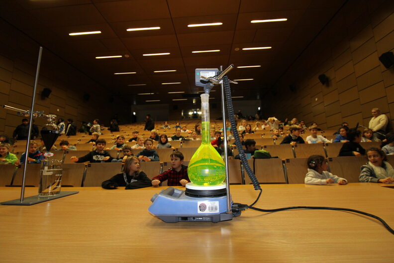 Während einer Vorlesung wird eine grünlich schimmernde Flüssigkeit in einem Glaskolben erklärt