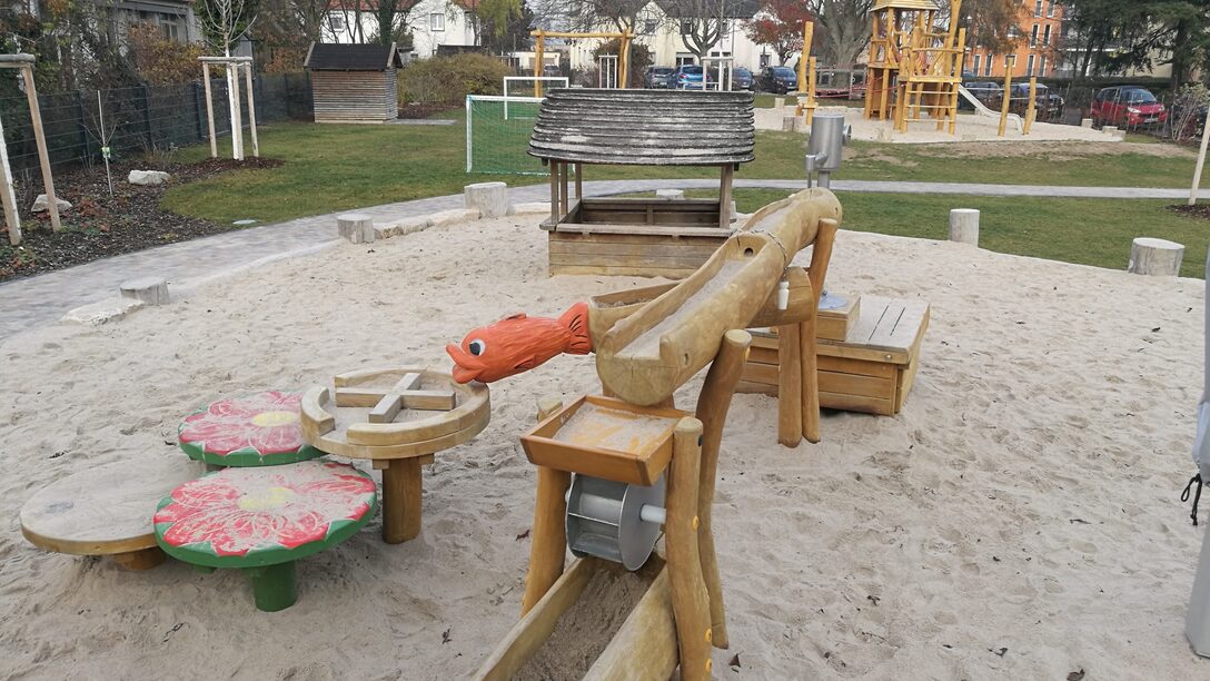 Das Außengelände der Kita Am Ehlenberg mit Sandspielfläche und Wasserspielgerät aus Holz